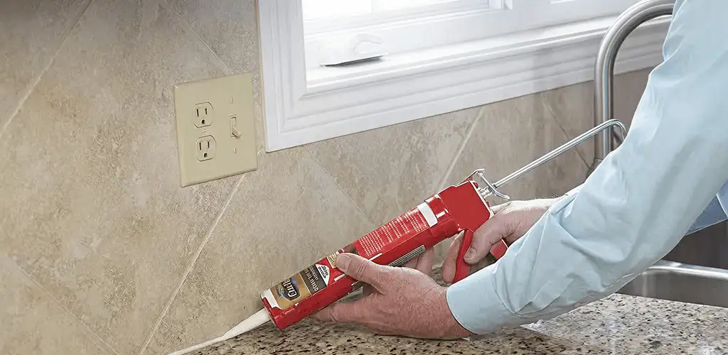 Handyman applying caulk along a kitchen backsplash and countertop seam in Honolulu, HI